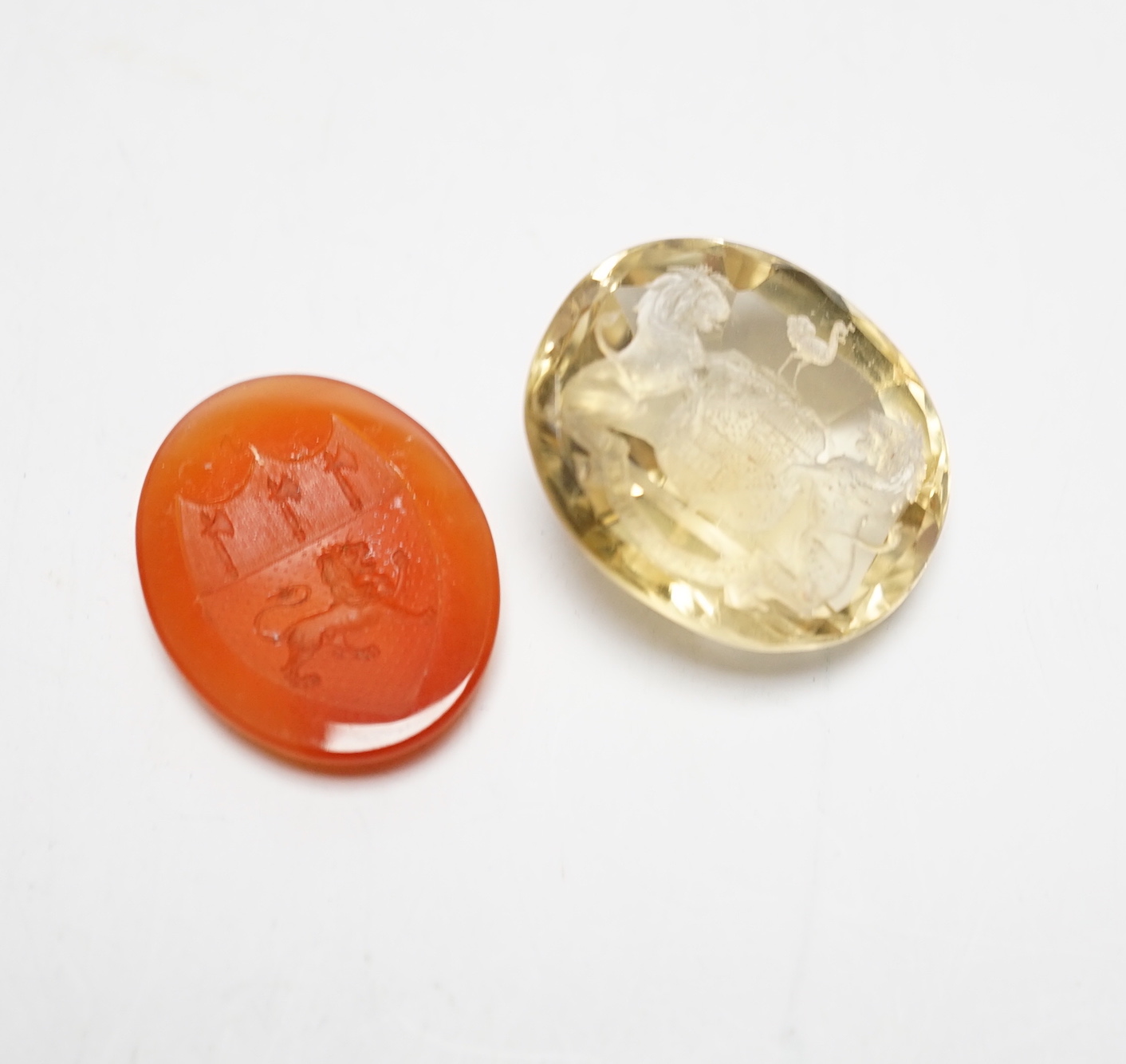 An unmounted oval cut intaglio citrine, 28mm by 25mm and a similar carnelian intaglio, both matrix carved with armorial/crest.